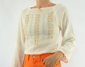 May include: A white embroidered blouse with a floral design and orange denim shorts.