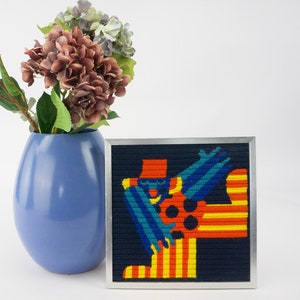 Peut inclure: Une œuvre d'art encadrée avec un motif abstrait coloré d'une personne portant un chapeau rouge et des vêtements bleus et jaunes. L'œuvre d'art est sur un fond bleu foncé et est encadrée en argent.