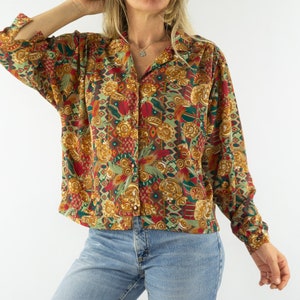 May include: A long-sleeved button-up shirt with a colourful, abstract print in shades of red, green, gold, and brown. The shirt has a relaxed fit and a collar.