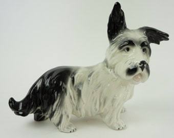 May include: A black and white ceramic figurine of a dog with a long, shaggy coat. The dog is standing on all four paws and has its head tilted to the side. The figurine is in good condition and has no chips or cracks.