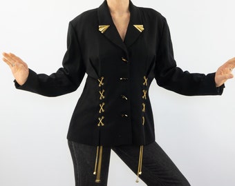 Puede incluir: Una chaqueta negra con detalles dorados y un detalle de encaje en la cintura. La chaqueta tiene cuello y mangas largas.