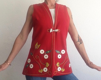 Pode incluir: Um colete vermelho sem mangas com um design floral bordado na frente. O colete tem uma guarnição dourada e um fecho de botão branco.