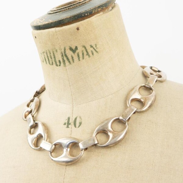 May include: A silver-toned chain necklace with large, oval links. The necklace is displayed on a mannequin with the word "STOCKMAN" and the number "40" visible. The background is plain white.