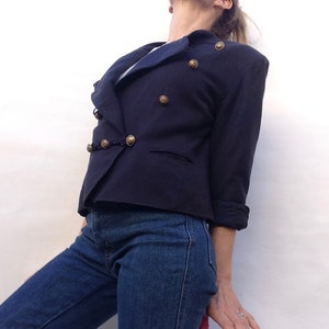 Pode incluir: Um blazer azul marinho com fecho de dupla abotoadura e bot&otilde;es dourados. O blazer tem colarinho e mangas compridas.