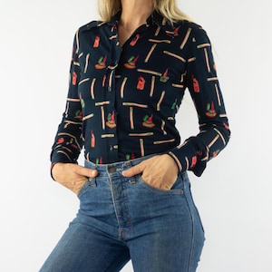 Puede incluir: Una camisa de manga larga azul marino con un estampado geométrico colorido. La camisa tiene un cuello abotonado y un corte holgado.