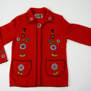 May include: Red wool jacket with embroidered floral designs. The jacket has a collar, long sleeves, and two pockets.