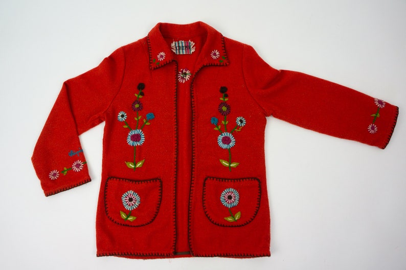 May include: Red wool jacket with embroidered floral designs. The jacket has a collar, long sleeves, and two pockets.