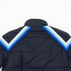 May include: A navy blue puffer jacket with a chevron pattern on the shoulders and sleeves. The chevron pattern is made up of white, light blue, and dark blue stripes.