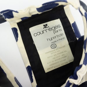 May include: A white and blue patterned fabric with a black label that reads "courreges paris hyperbole made in france".