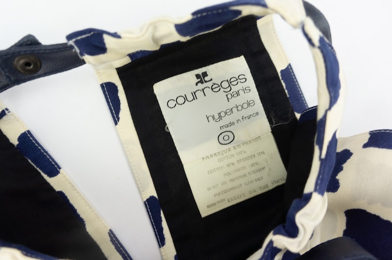 May include: A white and blue patterned fabric with a black label that reads "courreges paris hyperbole made in france".
