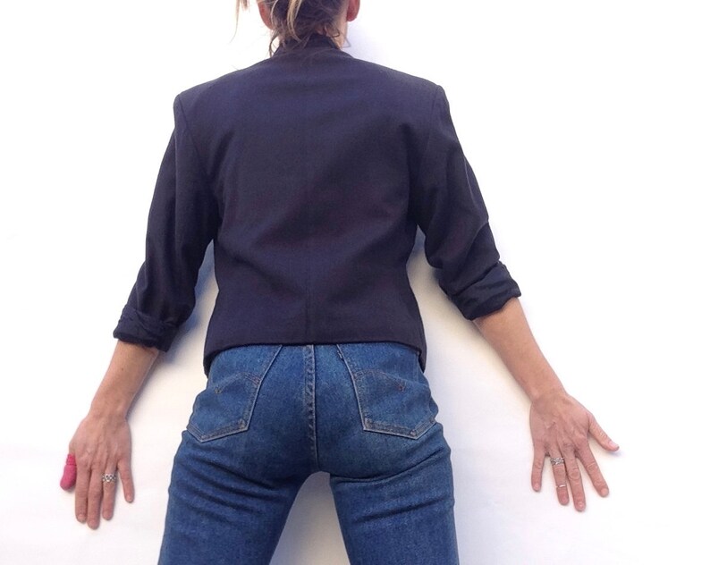 Pode incluir: Uma pessoa vestindo um blazer azul escuro e jeans azul. O blazer tem mangas compridas e gola.