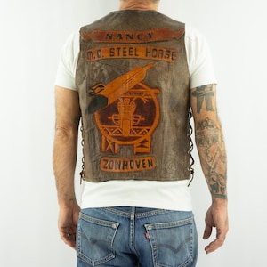 May include: Brown leather vest with the text "NANCY M.C. STEEL HORSE ZONHOVEN" and a motorcycle emblem. The vest has a distressed look with a lace-up side design.