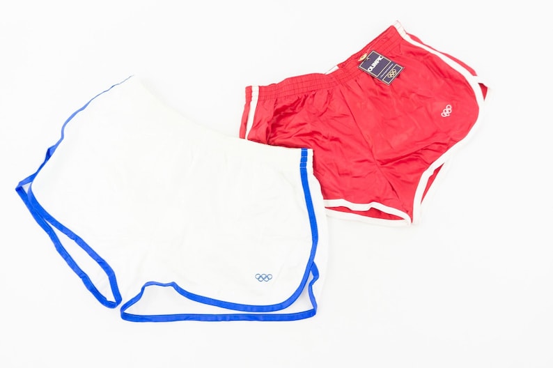 May include: Two pairs of athletic shorts, one white with blue trim and one red with white trim. Both pairs feature the Olympic rings logo.