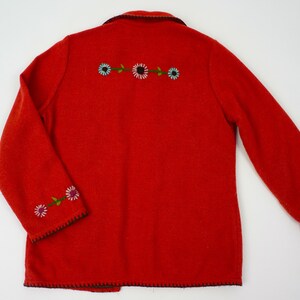 May include: Red wool jacket with embroidered flowers on the front and sleeves. The jacket has a black trim around the edges.
