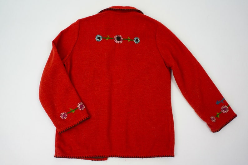 May include: Red wool jacket with embroidered flowers on the front and sleeves. The jacket has a black trim around the edges.