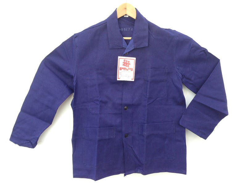 May include: A dark blue work jacket with a button closure and two large pockets on the front. The jacket has a label with the text "SPRZEDAŻ" on it.