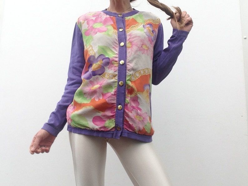 May include: A purple long-sleeved button-up shirt with a floral print. The shirt has a white background with orange, pink, and green flowers.