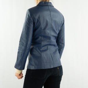 K&ouml;nnte beinhalten: Ein marineblauer Lederblazer mit klassischem Kragen und Knopfverschluss. Die Jacke hat lange &Auml;rmel und eine taillierte Passform. Der Blazer wird von hinten vor neutralem Hintergrund gezeigt.
