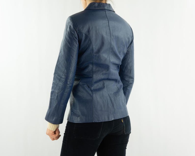 K&ouml;nnte beinhalten: Ein marineblauer Lederblazer mit klassischem Kragen und Knopfverschluss. Die Jacke hat lange &Auml;rmel und eine taillierte Passform. Der Blazer wird von hinten vor neutralem Hintergrund gezeigt.