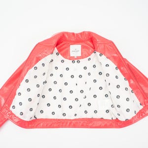May include: A pink leather jacket with a white polka dot lining. The jacket has a zipper closure and a collar.