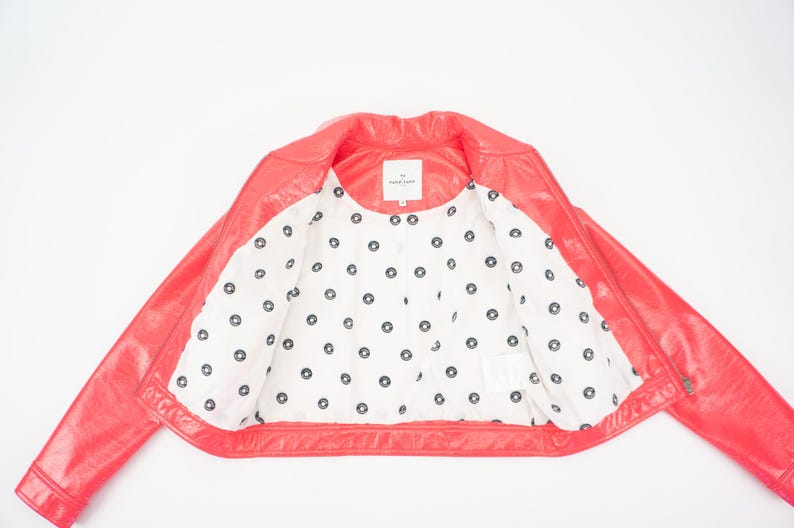 May include: A pink leather jacket with a white polka dot lining. The jacket has a zipper closure and a collar.