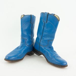 Könnte beinhalten: Ein Paar leuchtend blaue Cowboystiefel aus Leder mit wadenhohem Schaft, abgerundeten Zehenpartien und dunklen Ziernähten entlang des Schafts und Vorderblatts. Die Stiefel haben einen Blockabsatz und eine dunkelbraune Sohle im klassischen Schlupfdesign.