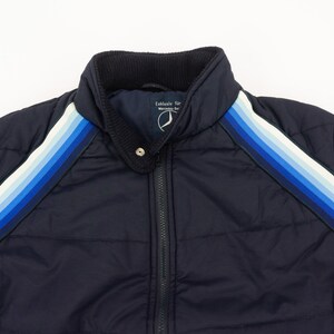 May include: A navy blue puffer jacket with a zipper closure and a white, blue, and light blue striped design on the shoulders.