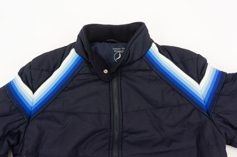 May include: A navy blue puffer jacket with a zipper closure and a white, blue, and light blue striped design on the shoulders.