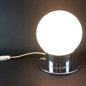 May include: A chrome table lamp with a white glass globe shade. The lamp has a round base and a cord with an inline switch.