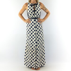 May include: A white maxi dress with a black and white geometric pattern. The dress has a sleeveless design and a keyhole neckline with a bow tie detail. The dress is belted at the waist.