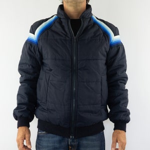 May include: A navy blue puffer jacket with a zipper closure and a ribbed knit collar, cuffs, and waistband. The jacket features a colorful striped design on the shoulders.