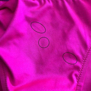 May include: Close-up of a bright pink fabric with three small, round, dark marks.