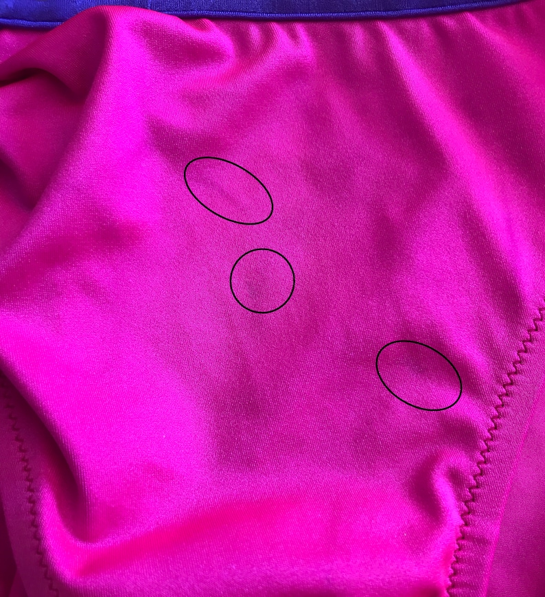 May include: Close-up of a bright pink fabric with three small, round, dark marks.