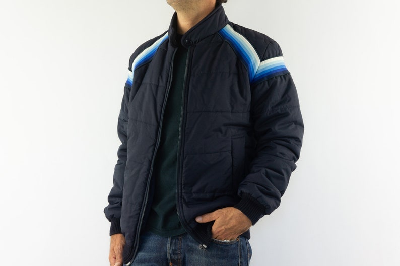 May include: A navy blue puffer jacket with a zipper closure and a colorful striped design on the shoulders.