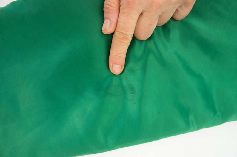 May include: Close-up of a green fabric with a small brown stain. The fabric is smooth and appears to be made of nylon.