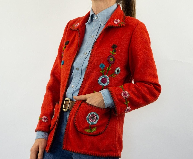 May include: A red jacket with floral embroidery. The jacket has a collar and pockets. The embroidery is in shades of blue, green, pink, and yellow.