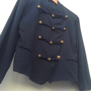 Pode incluir: Um blazer azul escuro com fecho de dupla abotoadura e bot&otilde;es dourados. O blazer tem um design &uacute;nico com guarni&ccedil;&atilde;o tran&ccedil;ada em torno dos bot&otilde;es.