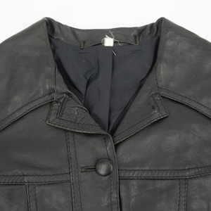 May include: Close-up of a black leather jacket with a large collar and a single button closure. The jacket has a classic design with visible stitching details and a tailored fit. The garment appears to be vintage.