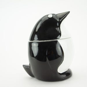 May include: A black and white ceramic penguin shaped cookie jar with a glossy finish.