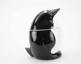 May include: A black and white ceramic penguin shaped cookie jar with a glossy finish.