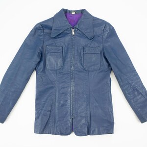 K&ouml;nnte beinhalten: Eine marineblaue Vintage-Jacke mit lila Futter. Die Jacke hat einen Kragen, zwei Vordertaschen und einen durchgehenden Rei&szlig;verschluss. Die lang&auml;rmlige Jacke ist aus Leder oder leder&auml;hnlichem Material.