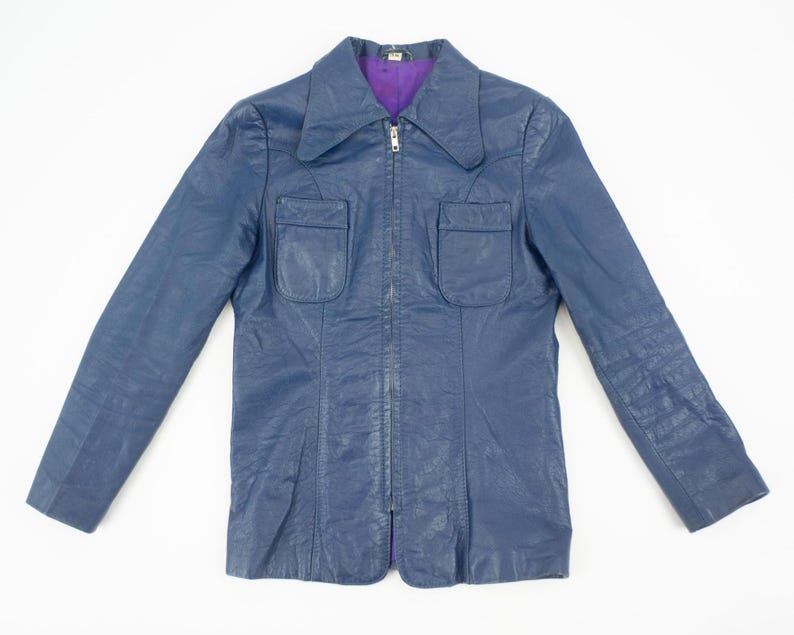 K&ouml;nnte beinhalten: Eine marineblaue Vintage-Jacke mit lila Futter. Die Jacke hat einen Kragen, zwei Vordertaschen und einen durchgehenden Rei&szlig;verschluss. Die lang&auml;rmlige Jacke ist aus Leder oder leder&auml;hnlichem Material.