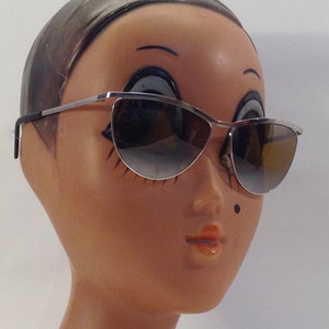 May include: Silver cat-eye sunglasses with brown gradient lenses on a mannequin head.