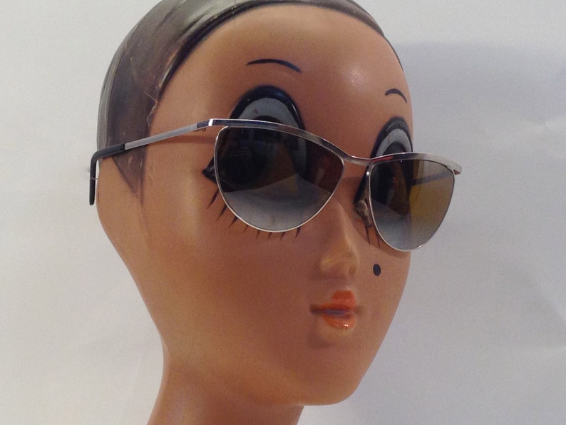May include: Silver cat-eye sunglasses with brown gradient lenses on a mannequin head.