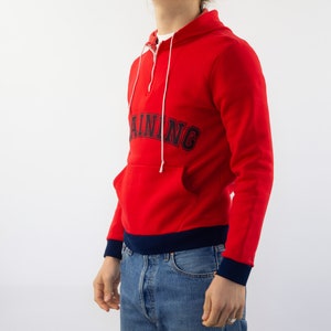 K&ouml;nnte beinhalten: Roter Kapuzenpullover mit einem dunkelblauen "TRAINING"-Logo auf der Vorderseite. Der Pullover hat einen halben Rei&szlig;verschluss und einen dunkelblauen Bund am unteren Rand.