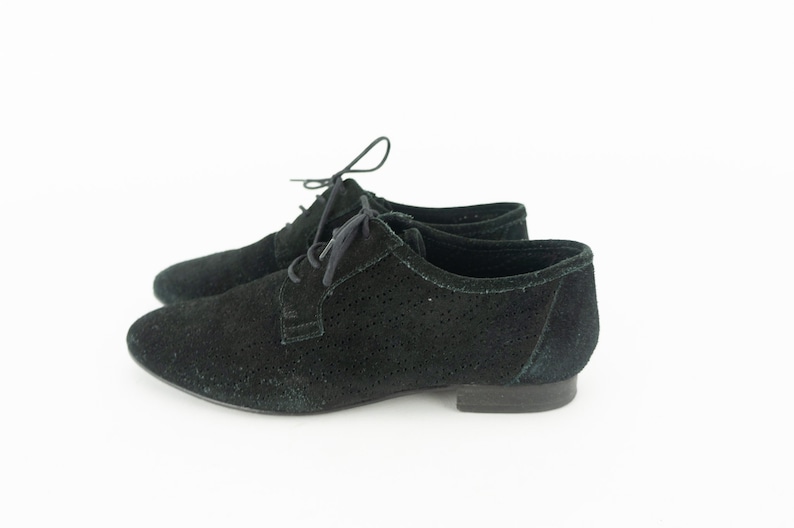 Op de afbeelding: Een paar zwarte su&egrave;de veterschoenen met een geperforeerd ontwerp.