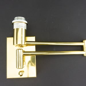 May include: A gold-toned wall-mounted light fixture with a single bulb socket and two adjustable arms. The socket is labeled "Max 100W".