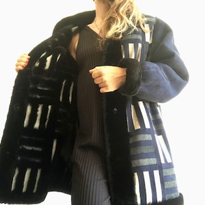 Puede incluir: Un abrigo de piel de oveja con estampado azul y gris con forro de piel negro. El abrigo está abierto y el forro es visible.
