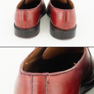 May include: A pair of burgundy leather lace-up shoes with black soles. The shoes are worn and have some scuffs and scratches.