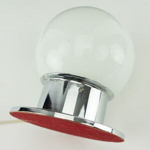 May include: A chrome table lamp with a large white glass globe shade. The base has a red felt bottom.